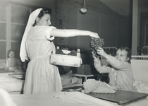 405224 Afbeelding van een zuster die druiven uitdeelt aan kinderen in een ziekenhuis of kindertehuis.